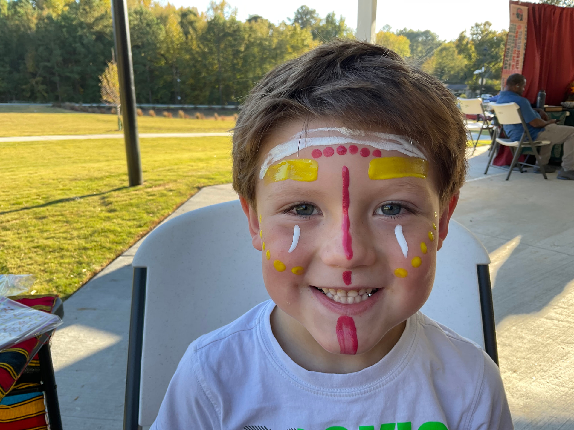 A smiling child showing their face painting at an outdoor community celebration